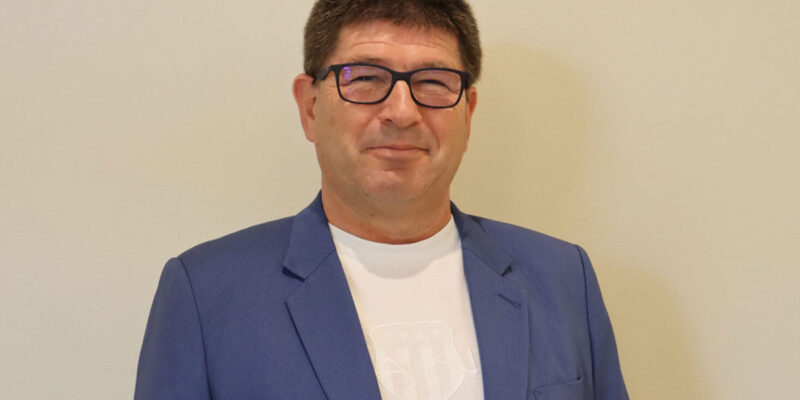 Mann im blauen Sakko vor einer hellen Wand. (Foto: AM)