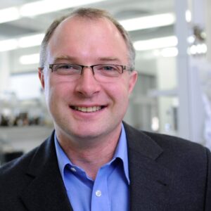 Mann im Anzug mit Labor im Hintergrund. (Foto: Gerd Grimm / FAU)