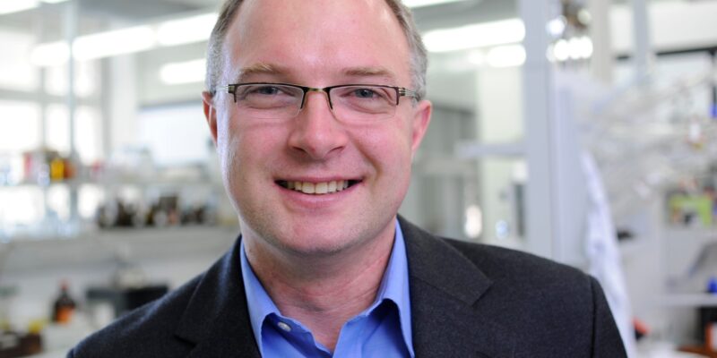 Mann im Anzug mit Labor im Hintergrund. (Foto: Gerd Grimm / FAU)