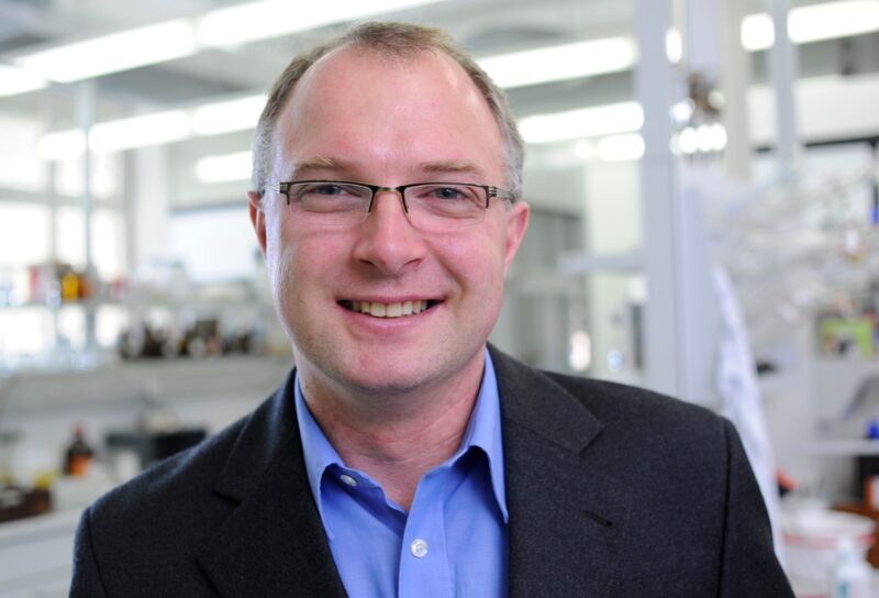 Mann im Anzug mit Labor im Hintergrund. (Foto: Gerd Grimm / FAU)