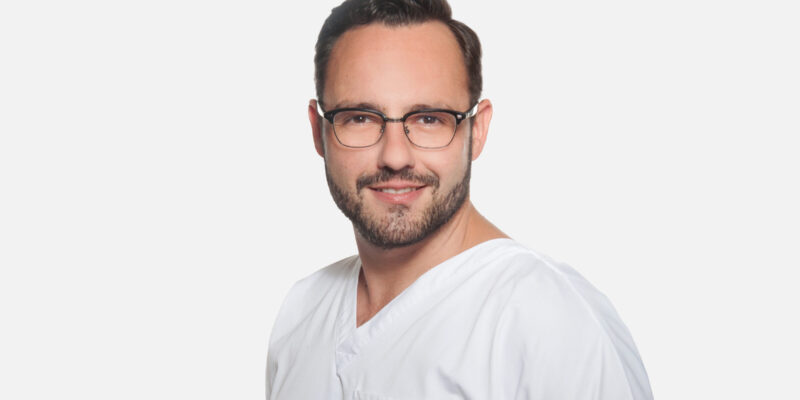 Mann in weißer medizinischer Kleidung vor weißem Hintergrund.