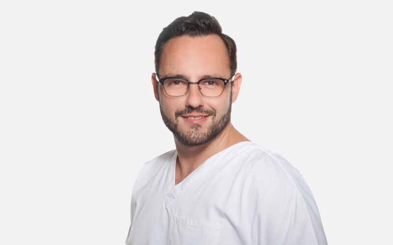 Mann in weißer medizinischer Kleidung vor weißem Hintergrund.