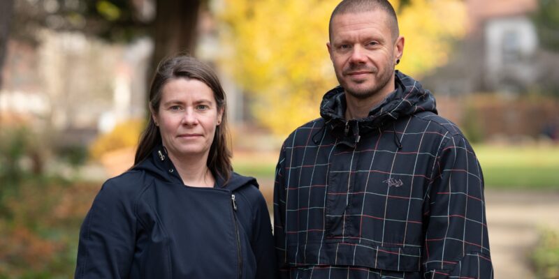 Mann und Frau in dunkler Kleidung draußen, Baum im Hintergrund