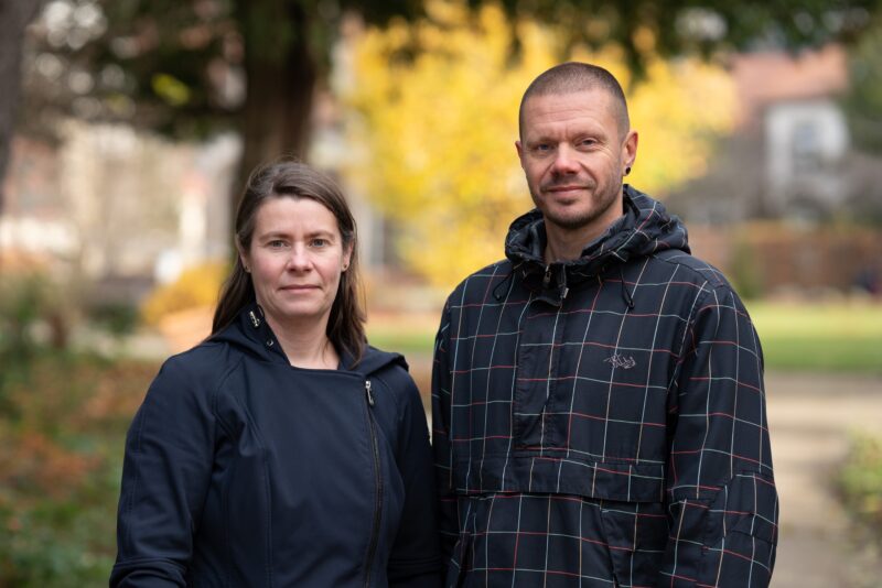 Mann und Frau in dunkler Kleidung draußen, Baum im Hintergrund